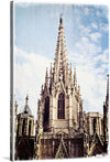 Capture the timeless beauty of Barcelona’s Gothic architecture with this exquisite print of the Barcelona Cathedral. The photograph, taken from a captivating low angle, showcases the cathedral’s intricate details and soaring spire against a serene pale blue sky. 