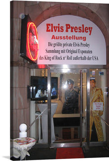  Step into the world of rock ‘n’ roll with this captivating print titled “Elvis Presley Ausstellung Düsseldorf (2012)”. This photograph captures the entrance to an Elvis Presley exhibition in Düsseldorf, Germany, marked by a vibrant red archway and a neon sign. 