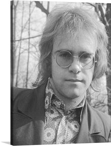  Step into a world of nostalgia and musical genius with our exclusive print, “Younger Elton John (1971).” This captivating piece captures an intimate moment of the iconic artist, adorned in his signature style that defined a generation. The grayscale tones evoke a sense of timeless elegance, while the intricate details of his attire tell a story of artistry and flamboyance. 