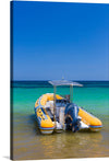 This vibrant print captures a moment of tranquility on a pristine beach. The focal point is a yellow inflatable boat, anchored close to the shore, equipped with an outboard motor and shaded by a small canopy. The calm turquoise sea transitions into a deep blue towards the horizon, under a clear azure sky. 