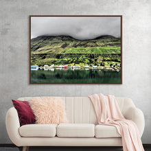  “Iceland with Clouds 1” by Julie Elliot is a captivating print that transports viewers to the serene landscapes of Iceland. The artwork masterfully captures the essence of a secluded village nestled amidst lush green mountains, their peaks gently veiled by low-hanging clouds. The reflective waters of a tranquil lake mirror this picturesque scene, while colorful houses dot the shoreline.