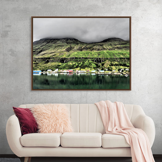 “Iceland with Clouds 1” by Julie Elliot is a captivating print that transports viewers to the serene landscapes of Iceland. The artwork masterfully captures the essence of a secluded village nestled amidst lush green mountains, their peaks gently veiled by low-hanging clouds. The reflective waters of a tranquil lake mirror this picturesque scene, while colorful houses dot the shoreline.