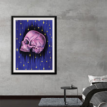  “Starry Night” by Marta Tesoro is a captivating artwork that seamlessly blends the macabre and the mystical. This exquisite print, encased in a sleek black frame, features a meticulously detailed skull rendered in haunting shades of purple, set against a cosmic backdrop of twinkling stars and cascading comets. Every brushstroke invites you into a universe where mortality and eternity converge, offering an enigmatic piece that is as thought-provoking as it is visually stunning. 